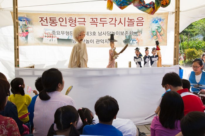 Children enjoy a <i>kkokdu</i> wooden puppet performance about the importance of having a good harvest, at the National Folk Museum of Korea.