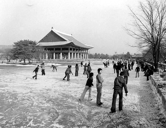 During winter 1975, kids and grownups enjoy skating while wearing only jeans and sweaters, at the frozen pond in front of the Gyeonghoeru Pavilion at Gyeongbokgung Palace.