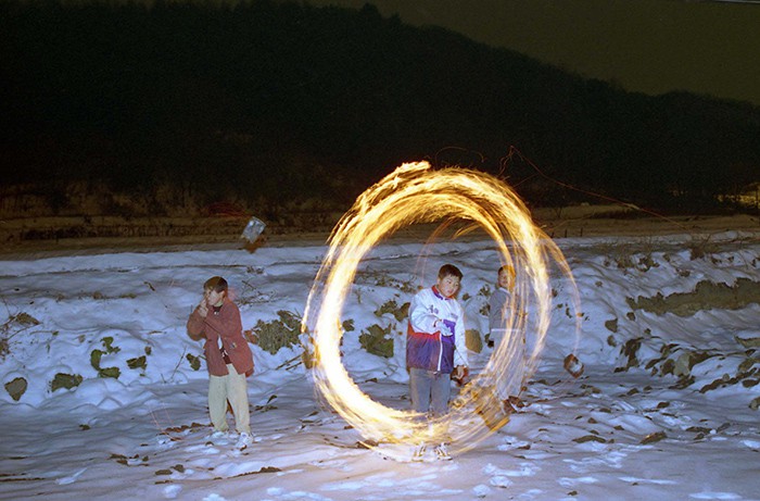 Kids enjoy a <i>jwibulnori</i> (쥐불놀이), a bundle of dried grass tied to a string and set on fire, on the night of Jeongwol Daeboreum in 1998. This folk game was used to help burn the fields and to remove mice and harmful insects from the farms before seeding, all in the hopes of having a good harvest.