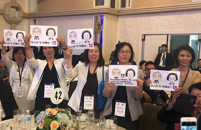 Korean residents pose for a photo holding up caricatures of President Moon Jae-in and first lady Kim Jung-sook, during a meeting between President Moon and Korean residents of Washington on July 1. (Cheong Wa Dae Facebook profile)