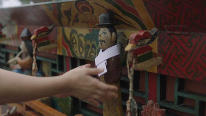 The wooden sculpture of caregiver kokdu is hung on grandmother’s bier.